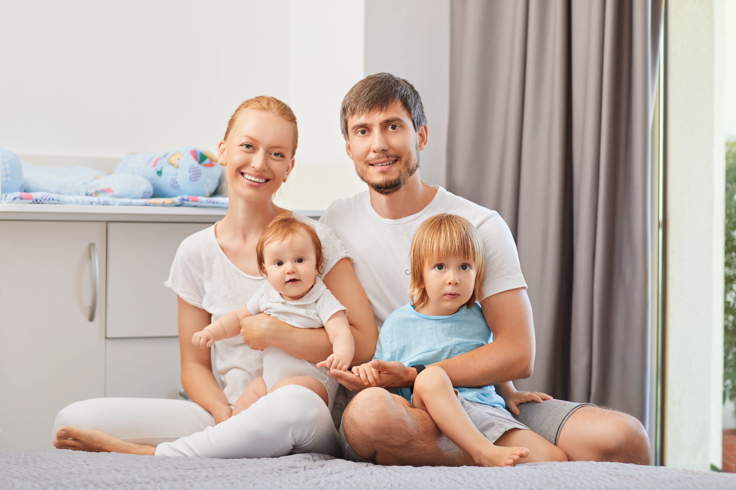 Happy,Family,With,Baby,On,Bed,Smiling,In,Room.